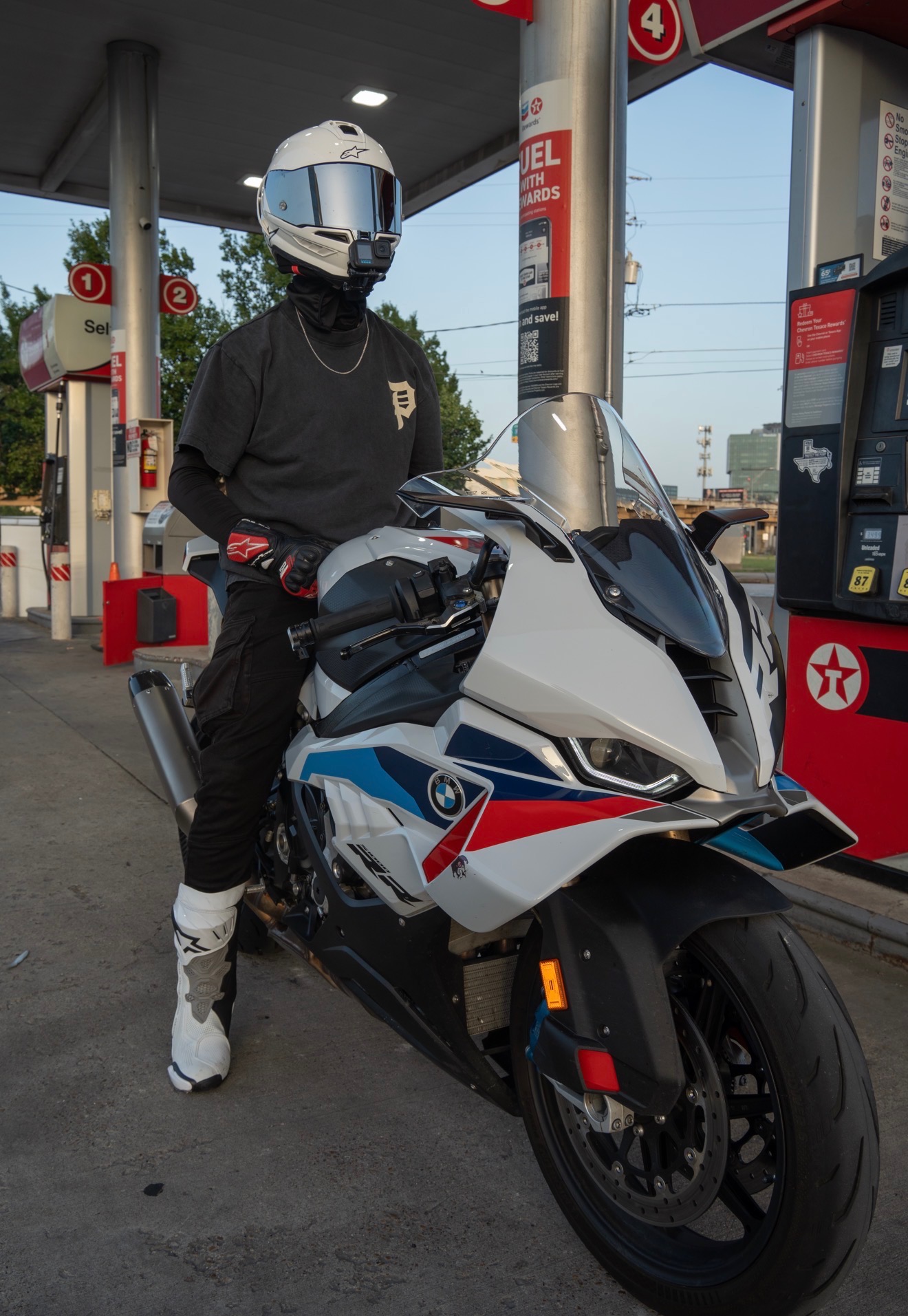 Blaze seated on his BMW S1000RR at a Texaco gas station at dusk.