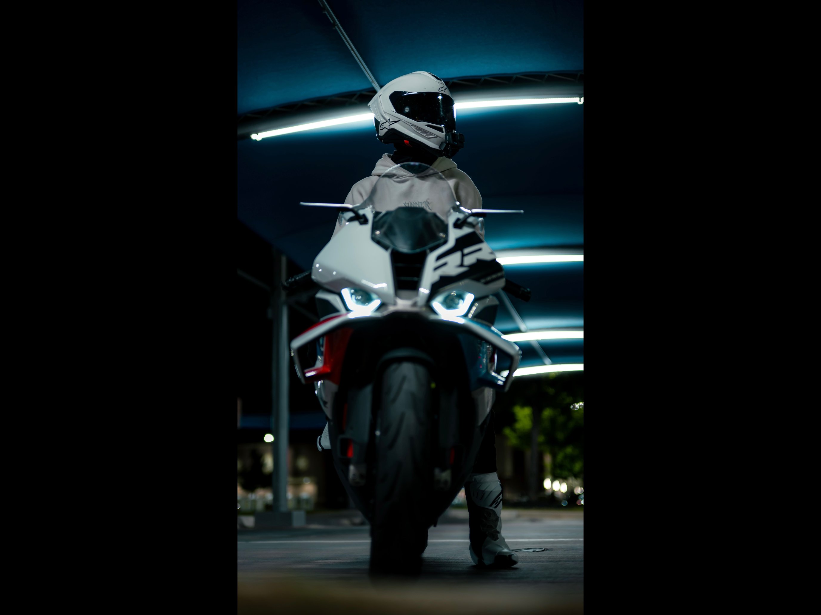 Blaze standing behind his BMW S1000RR at night, headlights on, garage lighting overhead.
